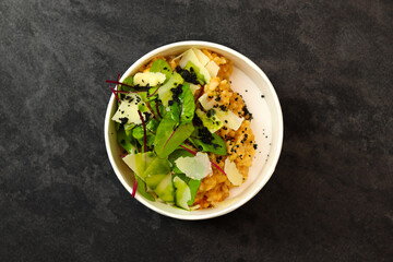Risotto with tomatoes, greens and parmesan in bowl on dark background. Restaurant dish delivery. Top view. Free space for text. Healthy food concept.