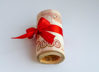 A bundle of Russian money tied with a red satin ribbon with a face value of 5000 rubles on a light background. The concept of finance, investment, savings and cash.