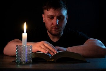 A man reads in the dark with a candle.