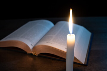 Candle with a book on the table in the dark.