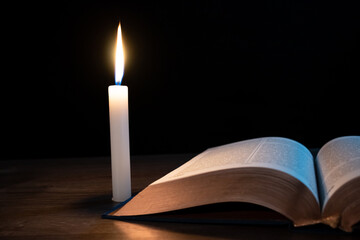 Candle with a book on the table in the dark.