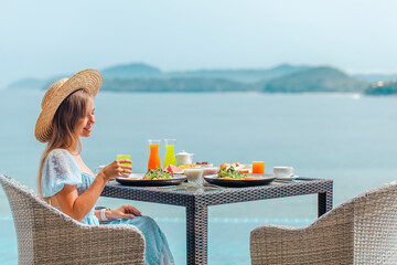 Woman in straw hat on summer vacation. Tropical resort and restaurant with sea view. Female traveler take a lunch or dinner in outdoor cafe with amazing ocean view. Weekend in hotel - obrazy, fototapety, plakaty