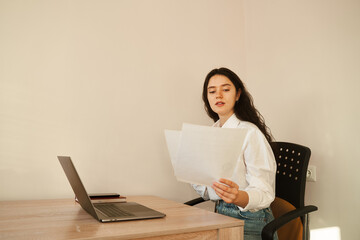 Attractive girl student holding papers and studying online using laptop at home. Online education and distance learning.