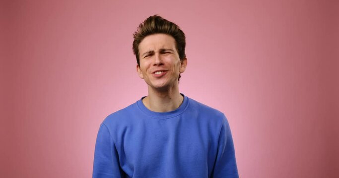 Disappointed young man regretting his deeds over pink background