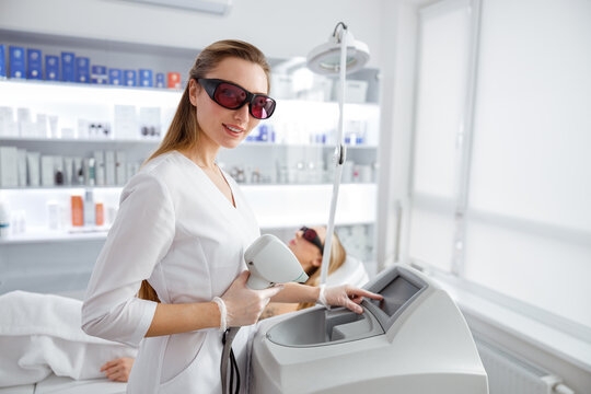Female cosmetologist using laser epilation machine in beauty salon
