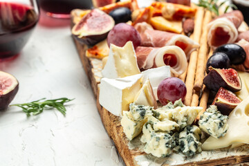 Assortment of cheese with prosciutto, honey, nuts and grape on cutting board. Cheese platter. Appetizers