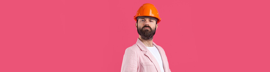 Portrait of young construction engineer wear orange hard hat, in a pink jacket standing on red studio background.