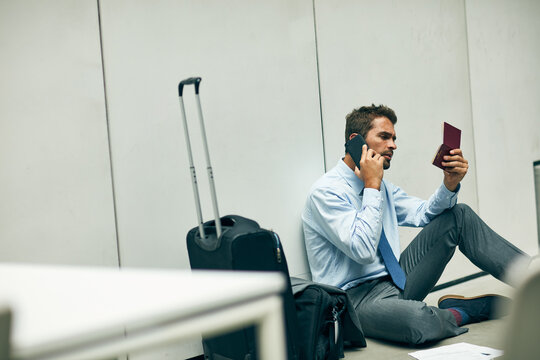 My permits have not expired. Cropped shot of a handsome young businessman sitting in an airport terminal and using his cellphone while holding his passport.