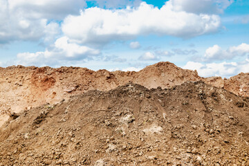 A pile of soil dug out of a trench against a blue cloudy sky. Earthworks at the construction site.