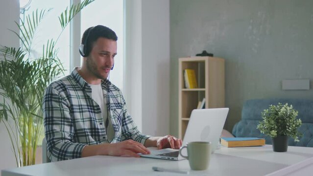 Call cente man wearing headset having presentation video call on laptop at his living room