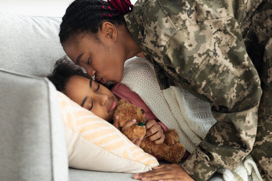 Black woman soldier leaving for military service, kissing sleeping daughter