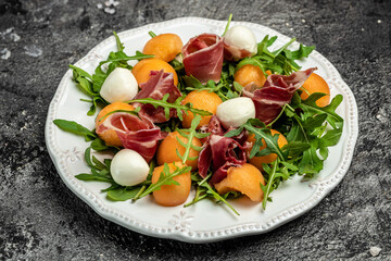 mediterranean salad with prosciutto or jamon, mozzarella and green basil leaves and Cantaloupe melon on white table, traditional Spanish and Italian appetizer served with wholemeal grissini, top view