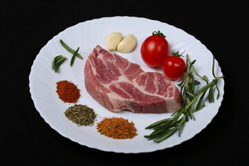 Fresh steak with spices and vegetables on a white plate and black background