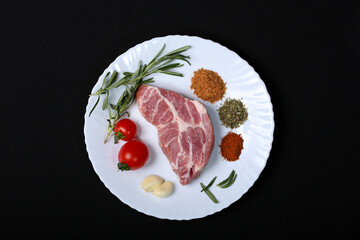 Fresh steak with spices and vegetables on a white plate and black background