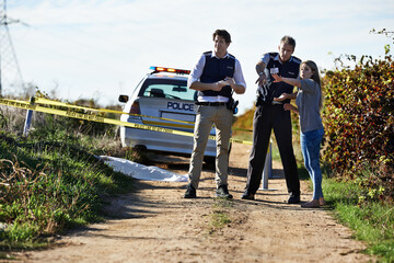 Getting her statement. Shot of a woman showing police officers where she found the body at a...