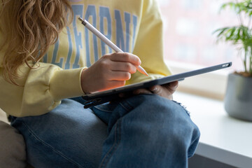 Close-up of teenage girl working on a tablet with white pencil. Online education, using gadgets.