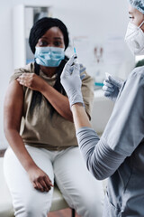 Close-up of female medic in protective gloves holding syringe for vaccination with patient sitting...