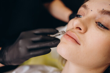 Crop of beautician in rubber gloves doing procedure lip augmentation for young beautiful woman in professional salon. Concept of beauty procedure with good mood.
