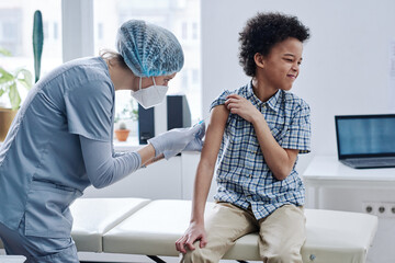 African little boy feeling pain while nurse giving an injection in his arm at hospital