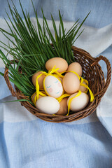 Painted Easter eggs, one egg with a cute face, eggs lie in a wooden basket along with green grass. Postcard for Easter.