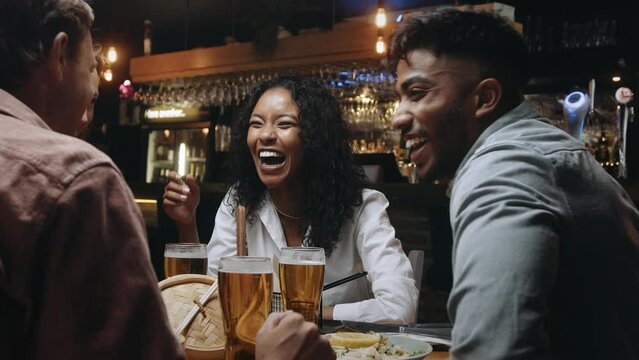 A multiracial woman having dinner and beers with a group of friends at a restaurant and laughing at something her friend said