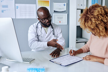 African male doctor in white coat suggesting his patient to sign medical agreement before operation