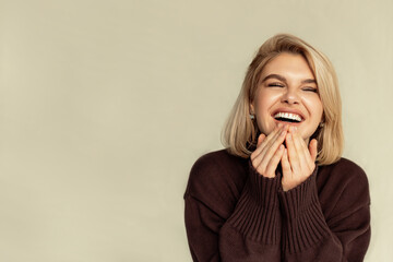 a shot of a joyful blonde with a short haircut, a young cute woman in a jumper laughs sincerely on...
