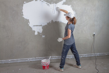 A woman makes a renovation in the house, a worker puts putty on a concrete wall