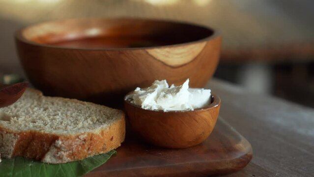 Traditional Russian fresh hot soup borsch with beetroot, red color, with sour cream and fresh bread in a wooden plate standing on a wooden table