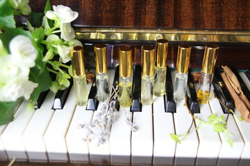 seven perfume aroma bottles with golden caps on piano keys on wooden classic piano with smell ingredients^ flowers, herbs, spice