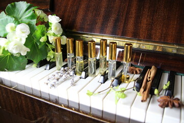 seven perfume aroma bottles with golden caps on piano keys on wooden classic piano with smell ingredients^ flowers, herbs, spice