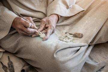 Close-up of artisan hands carving a stone souvenir or amulet for sale to tourists. Craft and...