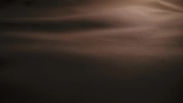 Flap of brown-gold fabric forms waves in slow motion. Macro. Texture.