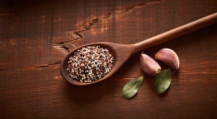 QuÃ­noa numa colher de madeira com temperos, alho e folhas de louro, em fundo de madeira