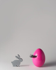 Pink Easter egg with false eyelashes and grey bunny on grey background. Beauty and make up concept. Spring, Easter minimal design. Copy space for text.