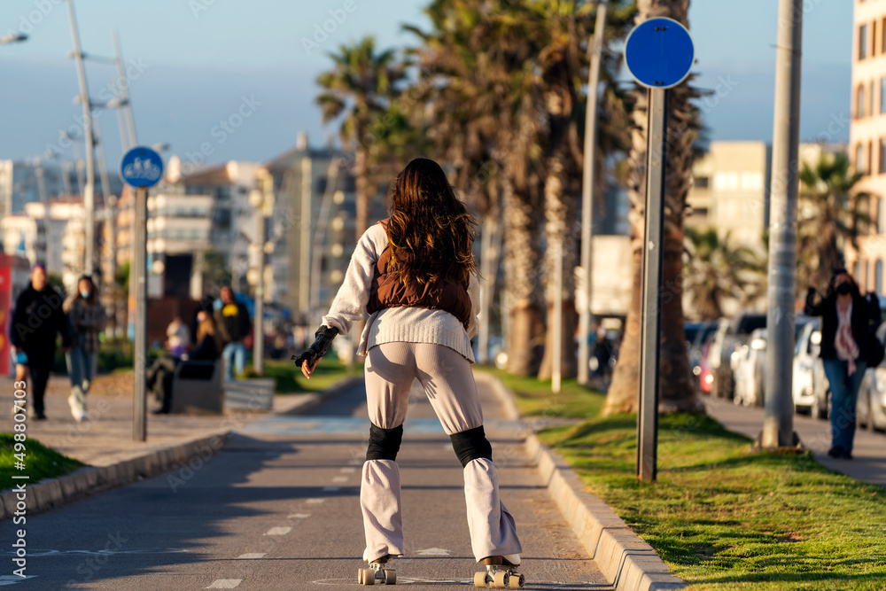 Wall mural unknown young woman roller skates down the street at sunset in la serena, back view