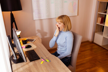 Woman yawning while sitting at her desk in an office