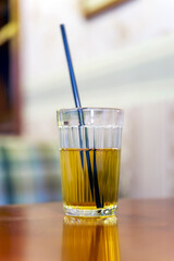 Apple juice in a faceted glass with a black straw on the table