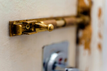 Old copper bolt on a white door with signs of destruction
