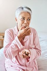 Oh yes, I definitely have a sweet tooth. Shot of a cheerful mature woman enjoying a piece of chocolate while being seated on a bed at home in the morning. - obrazy, fototapety, plakaty