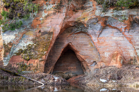 View to the Angels cave, a red sandstone cliff at the river Salaca in Skanaiskalns Nature Park in Mazsalaca in April in Latvia.