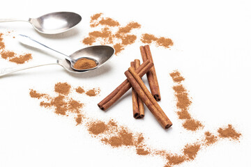 Cinnamon sticks among ground cinnamon, metal spoons on table.