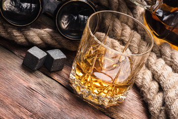 Whiskey in the drinking glass, bottle and mooring rope on the brown wooden table background.