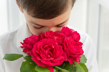 Little boy's face hiding into big bouquet of red roses on white background, greetings and celebration concept, copyspace.