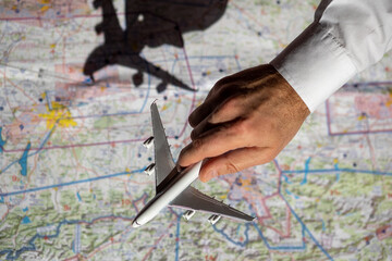 A pilot's hand holds a model aircraft over a navigation chart while making a flight plan. The shadow of the plane falls on the map. The concept of airlines.