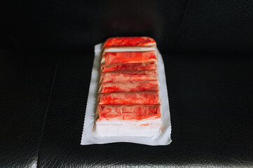 A package of frozen crab sticks, fish meat lies in a row on a black background.