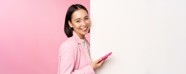 Image of korean female entrepreneur in suit, standing near info wall, advertisement on board,...