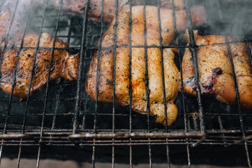 Chicken thighs are fried on the grill in a barbecue with smoke in nature.