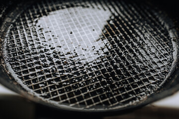 Background, texture, top view of a black frying pan with a checkered pattern, after cooking, smeared with sunflower oil. Photo of dirty dishes.