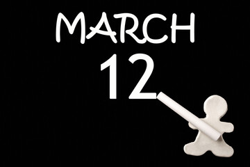 12th day of March. A small white plasticine man writing the date 12 March on a black board. Business concept. Education concept. Spring month, day of the year concept.